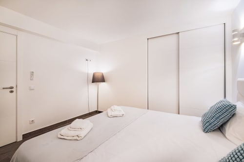 Quarto moderno no apartamento BlueHorizon SignatureStays em Albufeira com cama branca, guarda-roupa corrediço e luminária de pé
