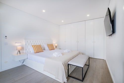 Quarto moderno no BlueHorizon by SignatureStays Albufeira com cama branca, almofadas listradas, TV e roupeiros do chão ao teto