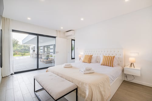 Quarto moderno no BlueHorizon by SignatureStays em Albufeira com roupa de cama branca, almofadas amarelas e acesso ao terraço