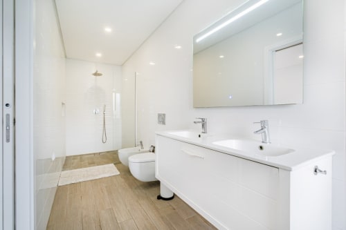 Casa de banho moderna no apartamento BlueHorizon SignatureStays em Albufeira com dois lavatórios, duche aberto e pavimento com efeito de madeira