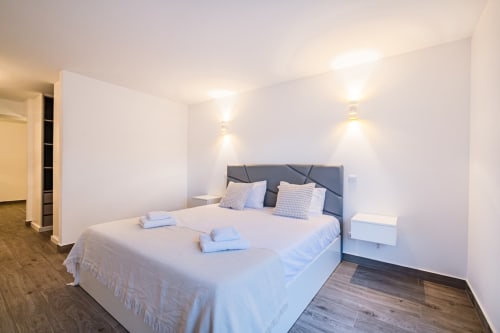 Quarto moderno no BlueHorizon by SignatureStays em Albufeira com cama de casal, cabeceira cinzenta, paredes brancas e iluminação acolhedora