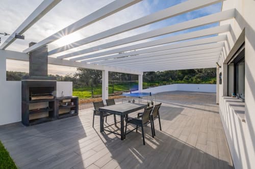 Terraço coberto moderno do apartamento BlueHorizon em Albufeira com mesa de jantar, lareira e vista para a piscina e jardim