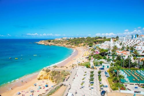 Vista aérea da Praia da Oura em Albufeira com águas turquesas, areia dourada, banhistas e apartamentos SignatureStays à beira-mar