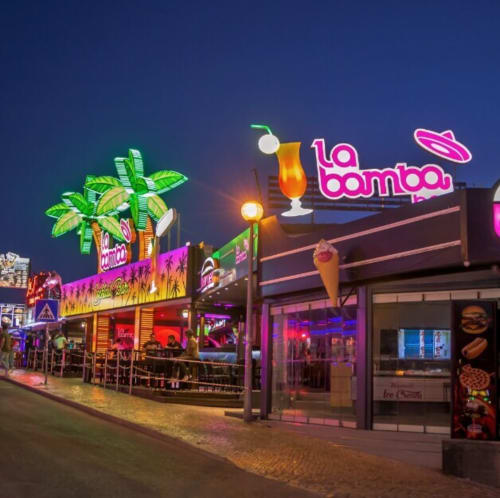 Vibrante venue 'La Bamba' com neon à beira-mar em Albufeira, decoração tropical e sinalética de coquetéis ao entardecer