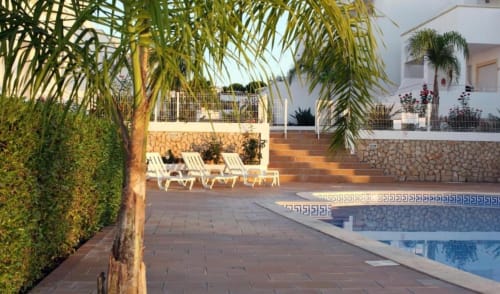 Zona de piscina do apartamento SignatureStays Farmvillage em Albufeira com espreguiçadeiras, palmeiras e edifício branco