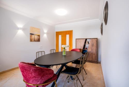 Sala de jantar moderna do apartamento SignatureStays Farmvillage em Albufeira com mesa oval preta e cadeiras de veludo rosa
