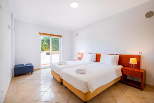 Quarto luminoso no SignatureStays Farmvillage, Albufeira com camas geminadas, acentos laranja e acesso à varanda