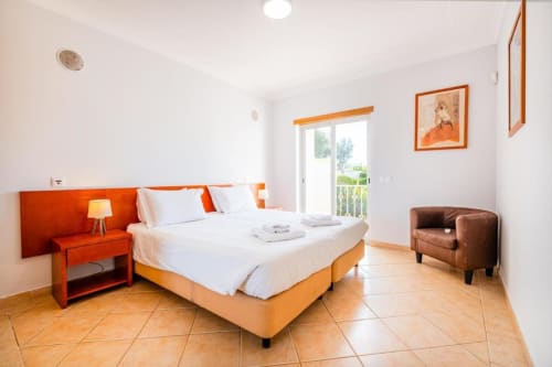Quarto luminoso na Farmvillage by SignatureStays em Albufeira com detalhes em laranja, pisos em terracota e acesso à varanda
