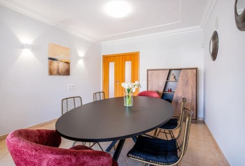 Moderna sala de jantar do apartamento Farmvillage em Albufeira com mesa oval preta, cadeiras em veludo rosa e portas de madeira