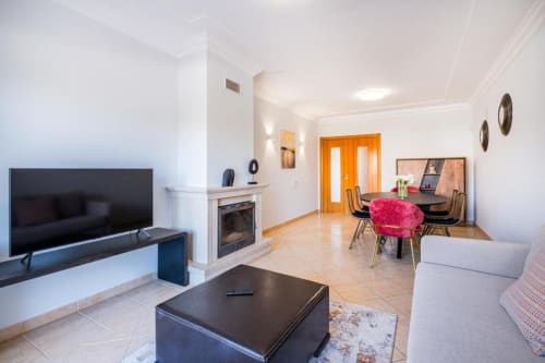 Sala de estar moderna em Albufeira com lareira, TV, área de refeições e portas laranja na SignatureStays