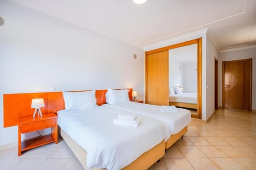 Quarto moderno e luminoso na Farmvillage SignatureStays Albufeira com detalhes em laranja, camas de solteiro e acabamentos em madeira