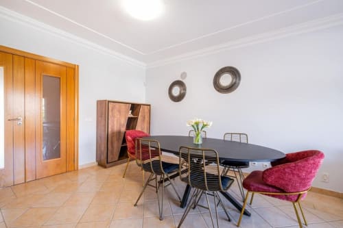 Moderna área de refeições no apartamento de Albufeira com mesa oval, cadeiras vermelhas, porta de madeira e pratos decorativos