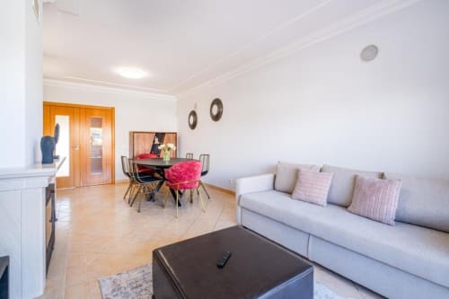 Sala de estar moderna com sofá cinzento, zona de refeições e portas de madeira na Farmvillage SignatureStays em Albufeira