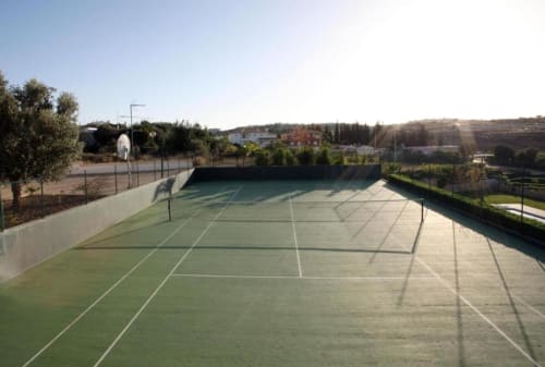 Quadra de ténis profissional na Farmvillage by SignatureStays em Albufeira, com cerca branca e paisagem rural envolvente