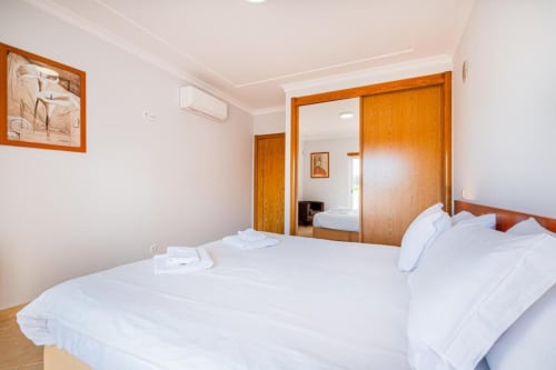 Quarto luminoso na SignatureStays Farmvillage em Albufeira com cama de casal, portas de madeira e comodidades modernas