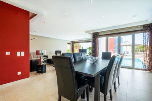 Área de jantar de apartamento moderno em Capetown Marina com mesa preta, parede em destaque vermelho e vista para a piscina em Albufeira