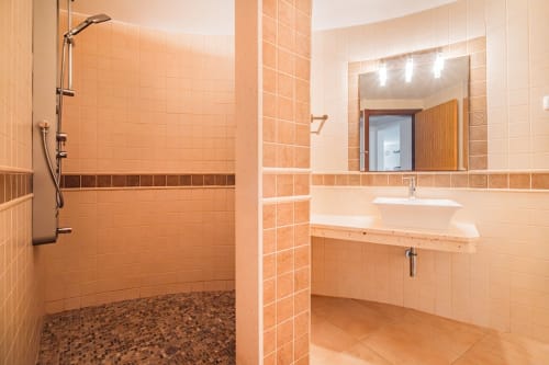 Banheiro moderno com azulejos laranja, chuveiro aberto, lavatório e espelho no apartamento Capetown Marina em Albufeira