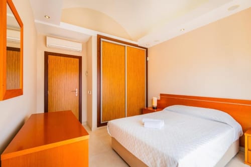 Quarto moderno na Marina de Albufeira com cabeceira laranja, roupa de cama branca e portas de madeira