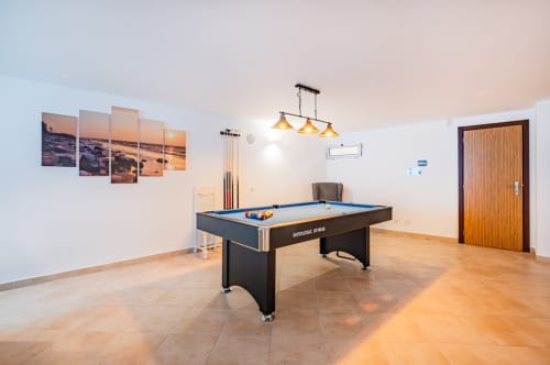 Moderna sala de jogos no apartamento Capetown Marina em Albufeira com mesa de bilhar, iluminação pendente e arte de pôr do sol na parede.