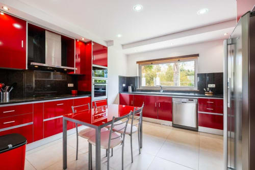Cozinha moderna vermelha com bancadas de granito preto, eletrodomésticos em aço inoxidável e área de refeições na Marina de Capetã