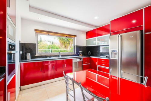 Cozinha moderna vermelha com eletrodomésticos em aço inox, painel traseiro preto e vista para o oceano no apartamento da Marina de Cidade do Cabo
