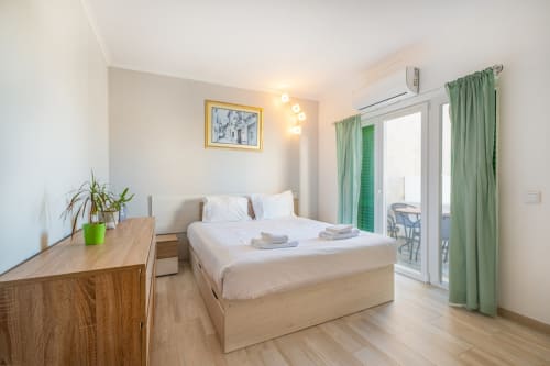 Quarto luminoso no Heart of Oura by SignatureStays em Albufeira com cama de madeira, secretária, cortinas verdes e acesso à varanda