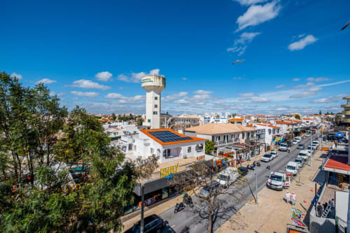 Vista aérea do apartamento Heart of Oura em Albufeira com painéis solares, caixa de água e rua movimentada abaixo