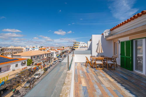 Terraço na cobertura com deck de madeira, mobiliário de jantar e sombrinha com vista para a rua de Albufeira no apartamento Heart of Oura