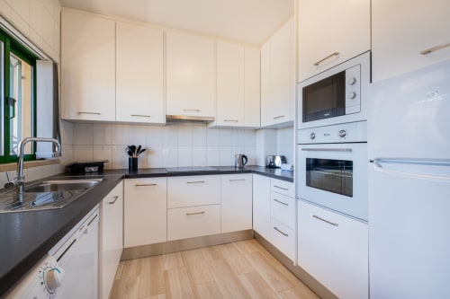 Cozinha moderna branca no apartamento Heart of Oura, SignatureStays Albufeira, com bancadas pretas e aço inoxidável