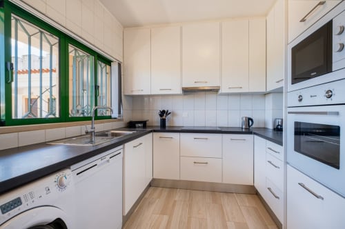 Cozinha moderna do apartamento Heart of Oura, Albufeira pela SignatureStays, com armários brancos e bancadas pretas