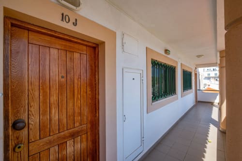 Corredor luminoso do apartamento Heart of Oura, Albufeira, com porta de madeira, paredes brancas e vista ensolarada.