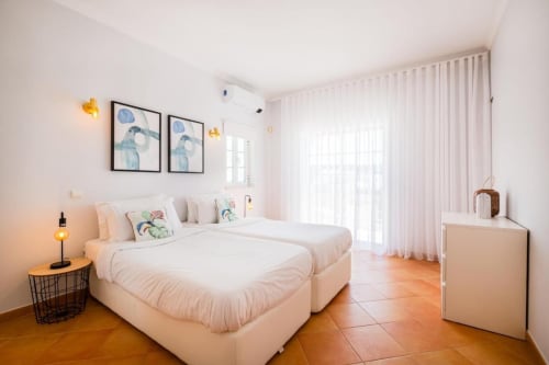 Quarto luminoso no apartamento SignatureStays Vicente Mar em Albufeira com camas gêmeas, cortinas brancas, piso em terracota