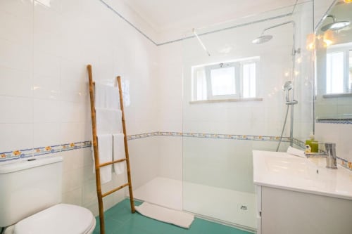 Casa de banho moderna no apartamento Vicente Mar em Albufeira com duche amplo, escada de toalhas em madeira e piso turquesa