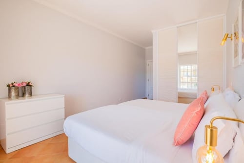 Quarto moderno no apartamento SignatureStays Vicente Mar em Albufeira com cama branca, almofada rosa, piso de madeira e espelho