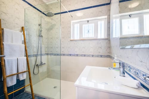 Banheiro moderno com chuveiro aberto, pia branca, detalhes em azulejos azuis e escada de toalhas em madeira no SignatureStays Vicente Mar,