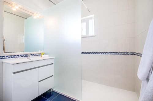 Banheiro moderno do apartamento Vicente Mar em Albufeira com penteadeira branca, box de vidro e detalhes em azulejo azul