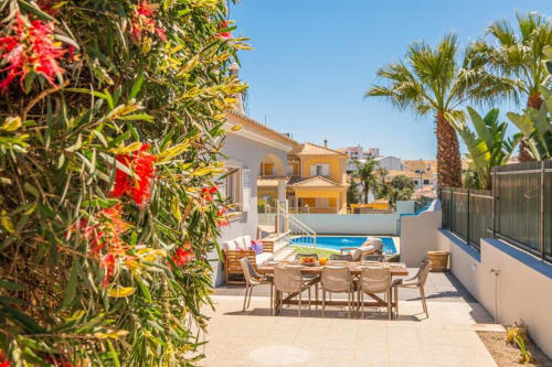 Terraço do apartamento SignatureStays Vicente Mar em Albufeira com piscina, zona de refeições e flores vermelhas vibrantes
