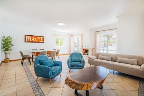 Apartamento moderno em Albufeira na Villa Rosal com poltronas azuis, sofá bege, mesa de madeira e sala de jantar com vista para o oceano