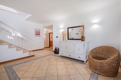 Entrada moderna e luminosa de villa com piso em azulejos, escada branca, cesta de vime e cômodas brancas com espelho em Albufeira