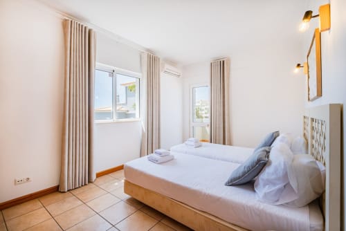 Quarto luminoso na Villa Rosal em Albufeira com duas camas de solteiro, cortinas bege e luz natural das janelas