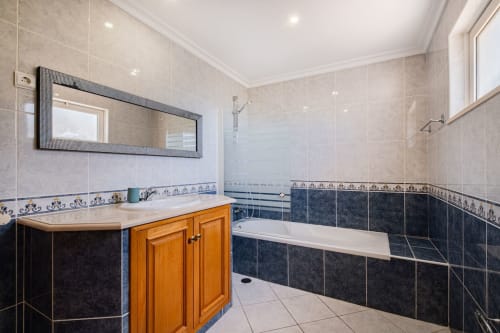 Banheiro moderno no apartamento Villa Rosal em SignatureStays Albufeira com revestimento em azulejo escuro, gabinete de madeira e banheira de imersão.