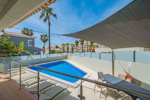 Área de piscina da Villa Rosal em Albufeira com piscina retangular azul, espreguiçadeiras, palmeiras e vista para o mar