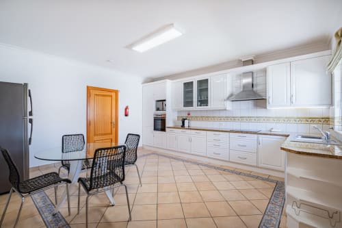 Cozinha moderna com armários brancos, área de refeições com cadeiras pretas e piso em azulejo bege na Villa Rosal by SignatureStays