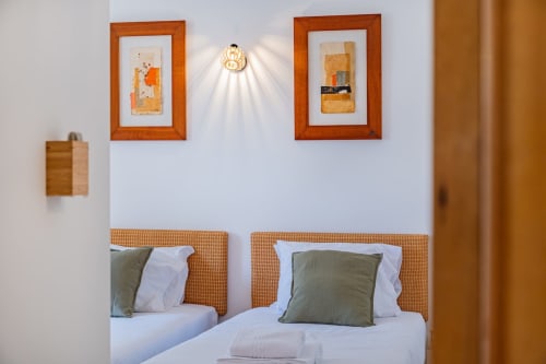 Quarto da Villa Rosal em Albufeira com camas gêmeas, cabeceiras trançadas em laranja e obras de arte emolduradas
