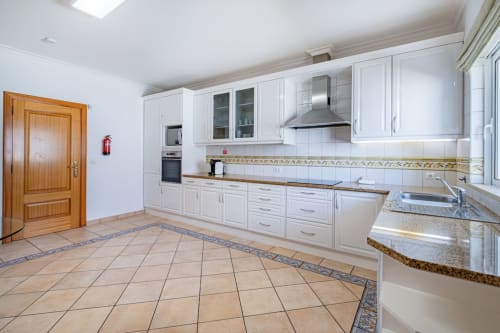 Cozinha moderna branca com bancadas em granito, eletrodomésticos em aço inoxidável e piso em cerâmica terracota na Villa Rosal, Albufeira