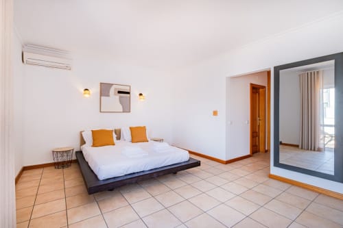 Quarto moderno da Villa Rosal by SignatureStays em Albufeira com cama branca, detalhes em laranja e acesso ao terraço