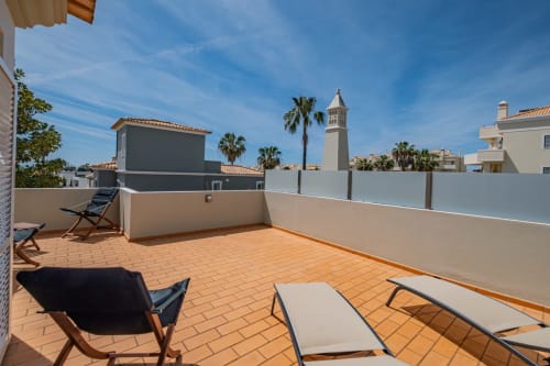 Terraço na cobertura da Villa Rosal em Albufeira com espreguiçadeiras, palmeiras e vista para a torre da igreja