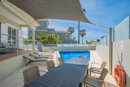 Área de piscina da Villa Rosal em Albufeira com espreguiçadeiras, mesa de refeições e vista para o mar sob vela de sombra
