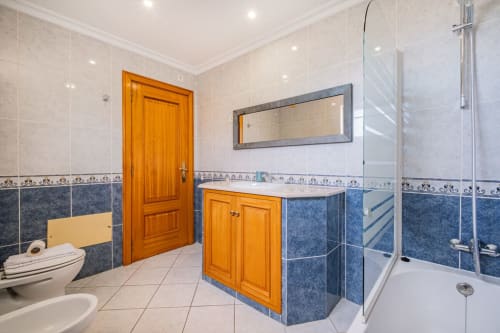 Banheiro moderno no apartamento Villa Rosal, Albufeira com detalhes em azulejos azuis, lavatório em madeira, chuveiro espaçoso e toalha aquecida
