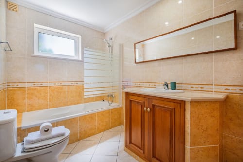 Banheiro moderno da Villa Rosal, Albufeira com azulejos laranja e bege, móvel em madeira, banheira e espelho